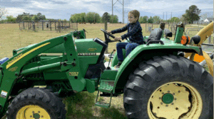 Child sitting on a green tractor outdoors.