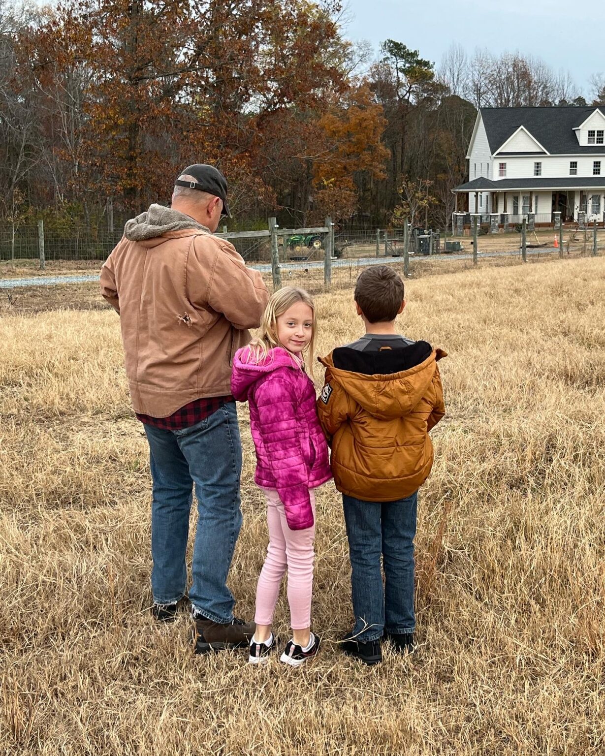 Father with two children in a field near a large house.