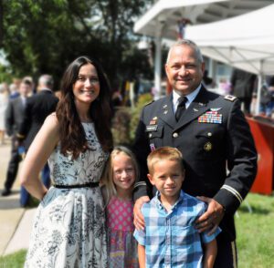 A family portrait with a man in military uniform and two children outdoors.