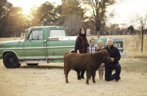 Family posing with a calf in front of a vintage green truck outdoors.