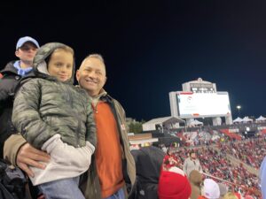 A man and a child at a crowded outdoor sports stadium at night.